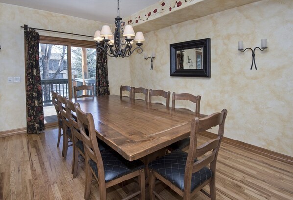 Une salle à manger avec une table et des chaises en bois, un lustre, un miroir et un balcon avec des rideaux.