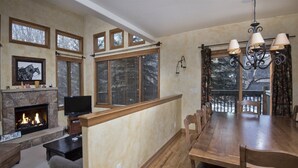 A spacious living room with a fireplace, a television, and a dining area with a long wooden table and chairs. - Millers Creek Resident (Edwards)