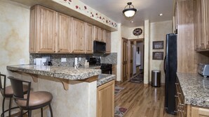 A kitchen with wooden cabinets, granite countertops, a black refrigerator, and a microwave. - Millers Creek Resident (Edwards)