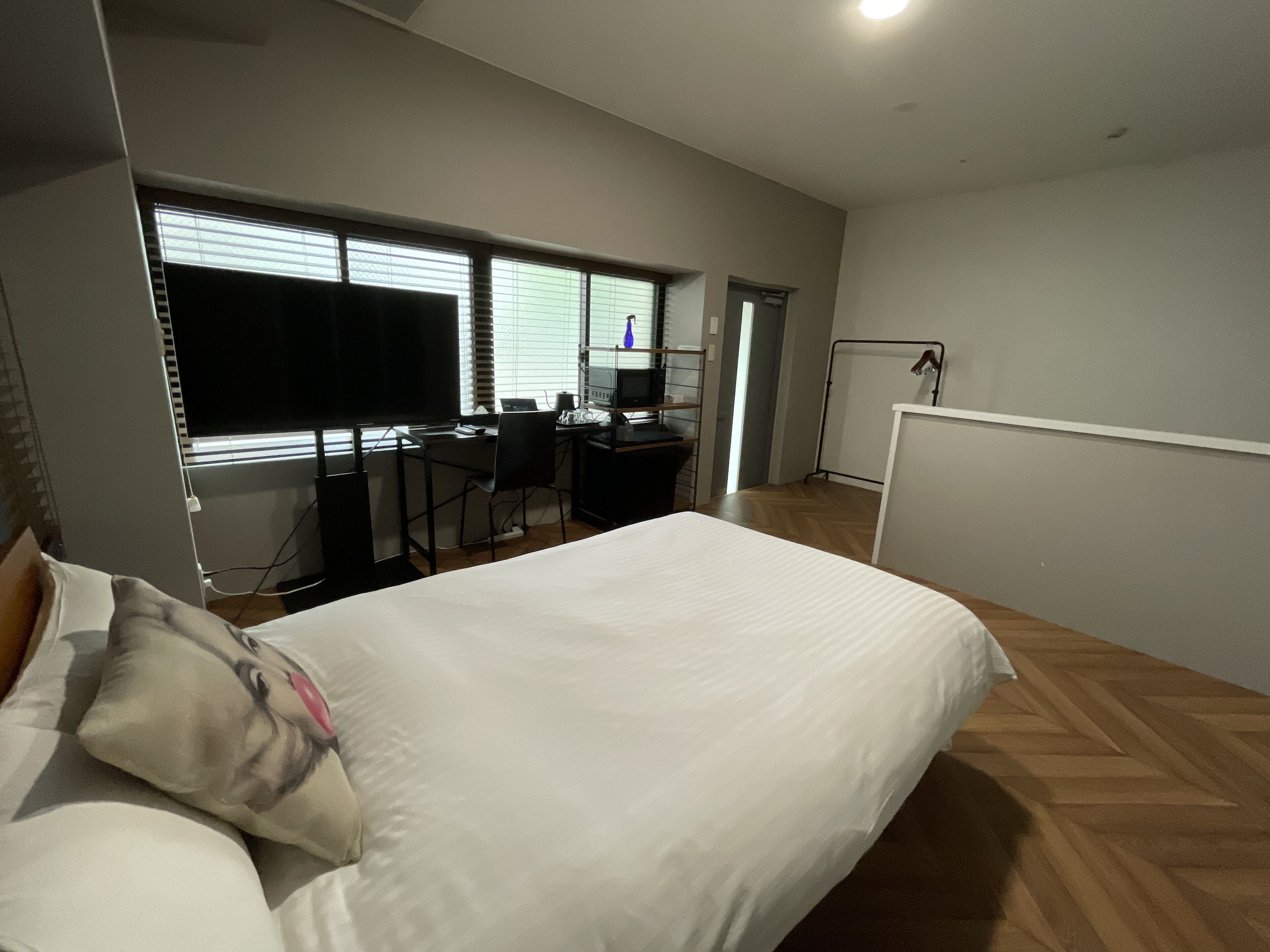Une chambre avec un lit, un bureau et une chaise. Il y a une fenêtre avec des stores, un radiateur et un tableau blanc fixé au mur.