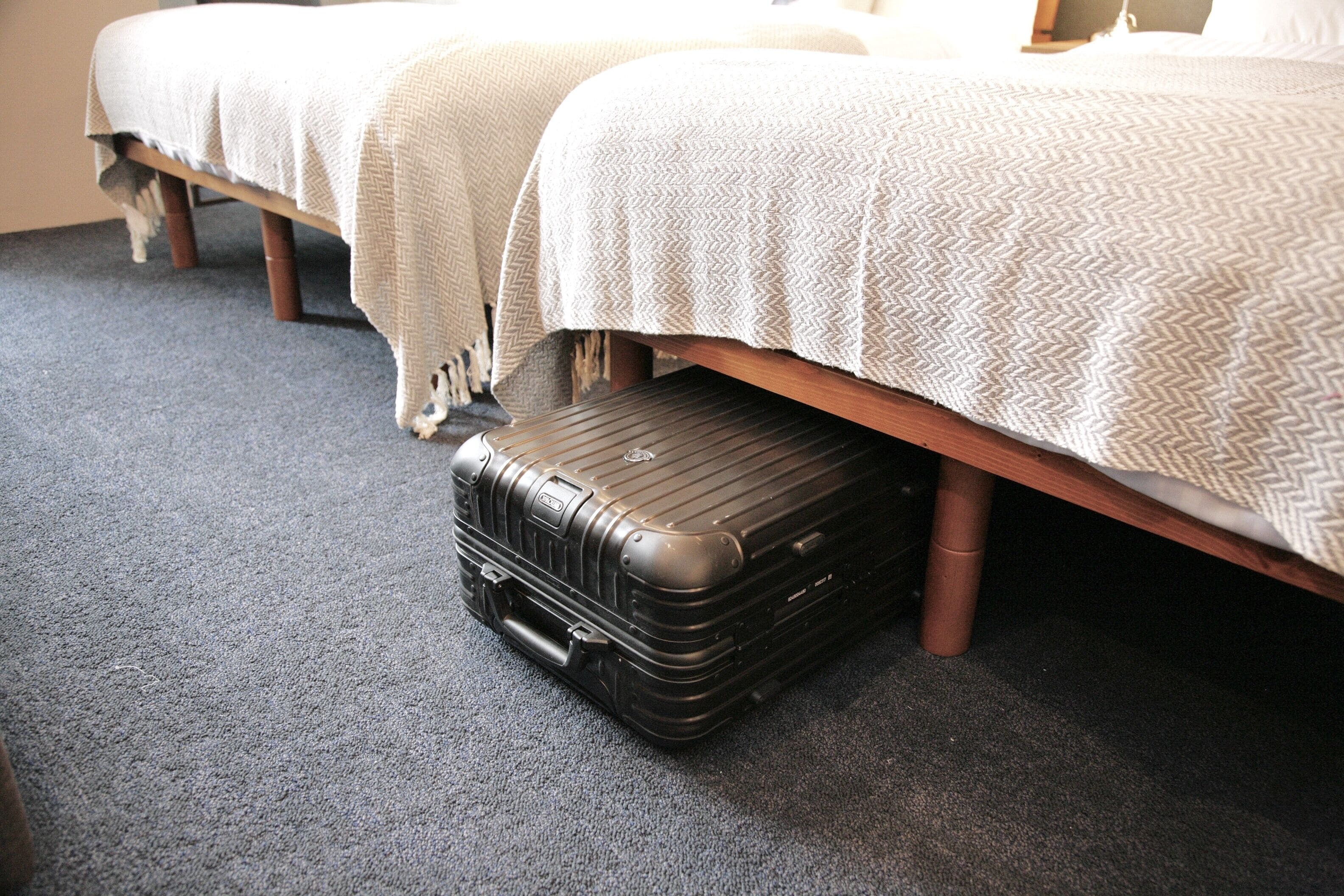 Een hotelkamer met twee bedden, een houten vloer en een zwarte koffer op de vloer.