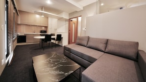 A modern living room with a sectional sofa, a marble coffee table, and a dining area with a small table and chairs. - Zonk Hotel Nakasu (Fukuoka)