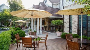 A patio with wooden furniture and umbrellas, surrounded by a brick building and greenery. - King's Garden Villa (Tainan)