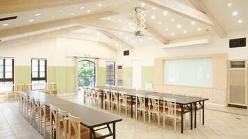 A spacious hall with long tables and chairs, high ceilings with exposed beams, and a large screen on one wall.
