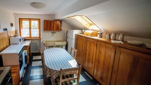 A compact kitchen with wooden cabinets, a table with a checkered tablecloth, and a window providing natural light. - Serrada di Folgaria, the attic of Villa Gentilini (Serrada)