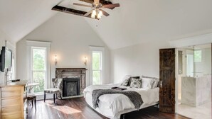 A spacious bedroom with a large bed, a fireplace, a ceiling fan, and a view of the outdoors through large windows. - The Waverly - Less than 2mi from Downtown (Nashville)