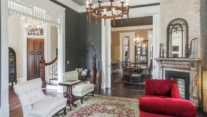 A spacious living room with a red armchair, a white armchair, and a chandelier. There is a dining area with a fireplace and a mirror above it. - The Waverly - Less than 2mi from Downtown (Nashville)