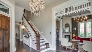 A spacious living area with a grand staircase, a fireplace, and a red sofa. - The Waverly - Less than 2mi from Downtown (Nashville)