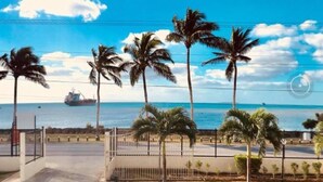 A coastal view with palm trees, a clear sky, and a ship in the distance. - Villa Ishadora (Nuku'alofa)