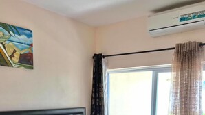 A hotel room with a bed, a window with curtains, an air conditioning unit, and a painting on the wall. - Villa Ishadora (Nuku'alofa)