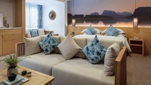 Une chambre d’hôtel moderne avec un grand lit, un canapé et une vue sur un lac au coucher du soleil.