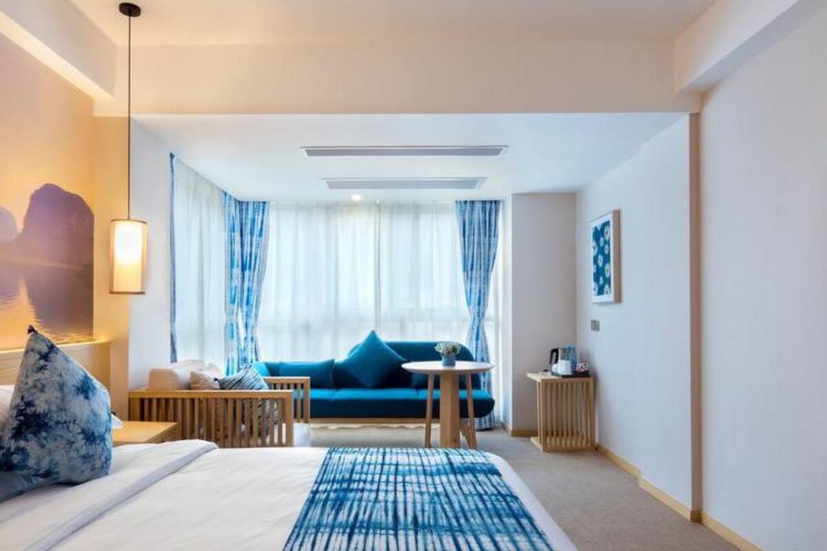 Une chambre d’hôtel avec un lit, un canapé bleu, une petite table et une fenêtre avec des rideaux.