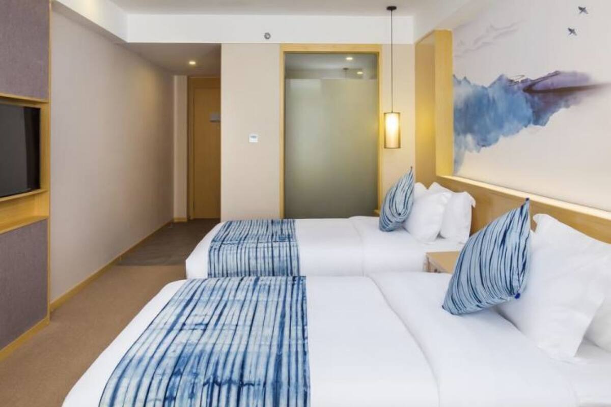 Une chambre d’hôtel avec deux lits, un grand tableau au mur et un téléviseur sur le côté gauche.