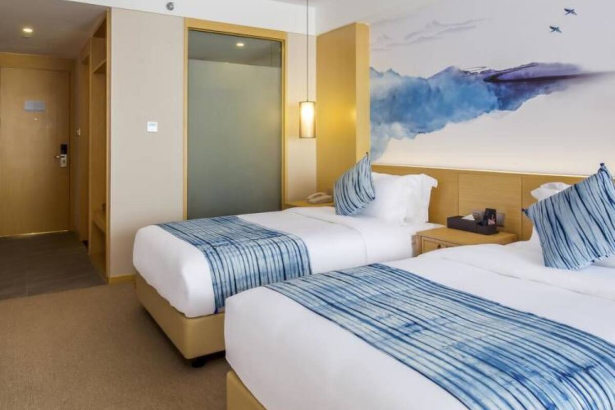Une chambre d’hôtel avec deux lits, un tableau représentant une vague bleue et une porte donnant sur un couloir.