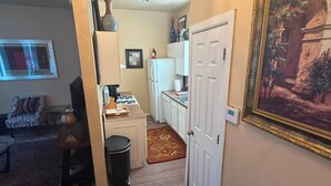 Un'area pranzo con tavolo, sedie, un lampadario, una cucina con pensili, un frigorifero e un quadro appeso al muro.