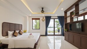 A hotel room with a large bed, a flat-screen TV, a ceiling fan, and a view of the outdoors. - Phuc Hung Riverside Villa (Da Nang)