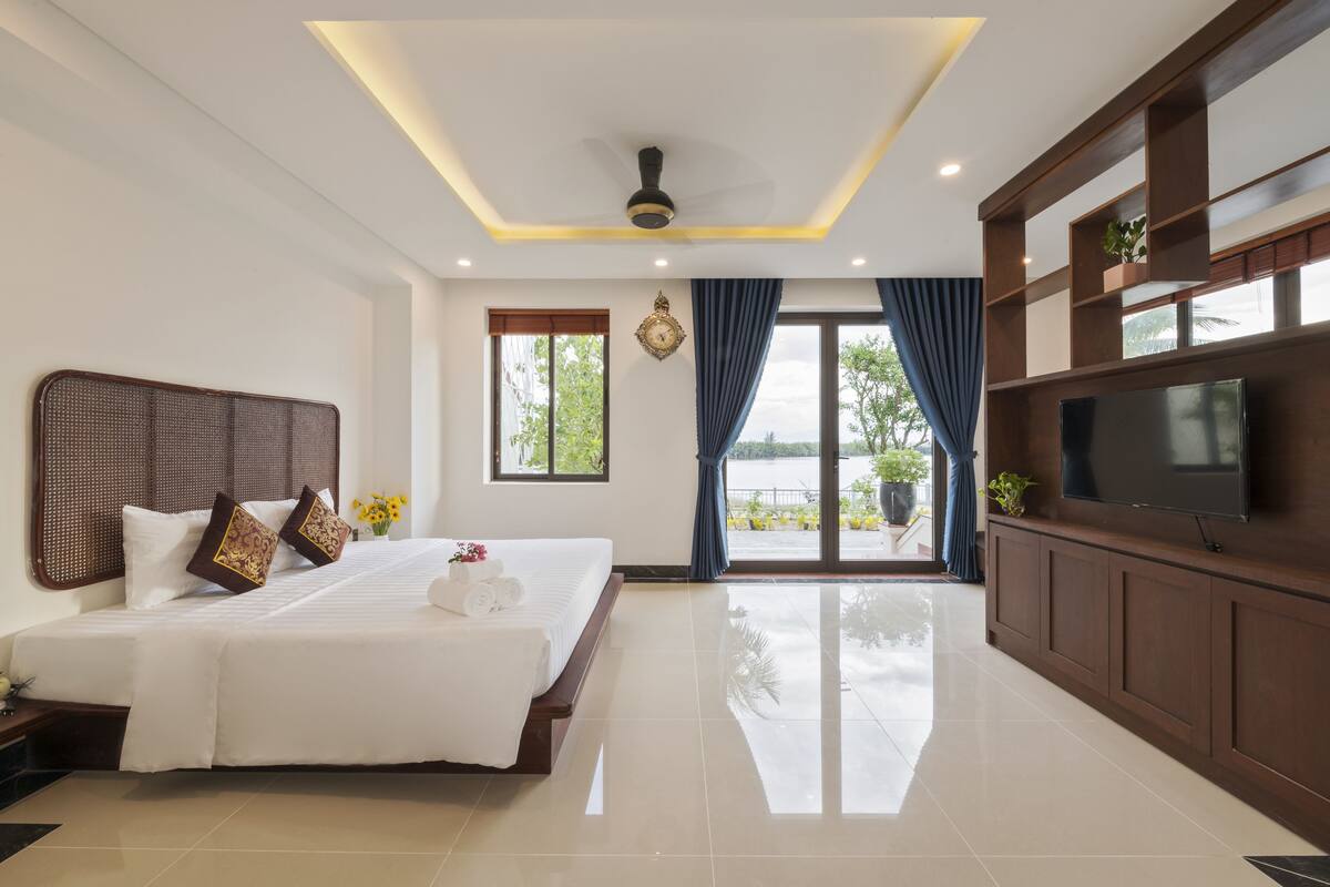 A hotel room with a large bed, a flat-screen TV, a ceiling fan, and a view of the outdoors.