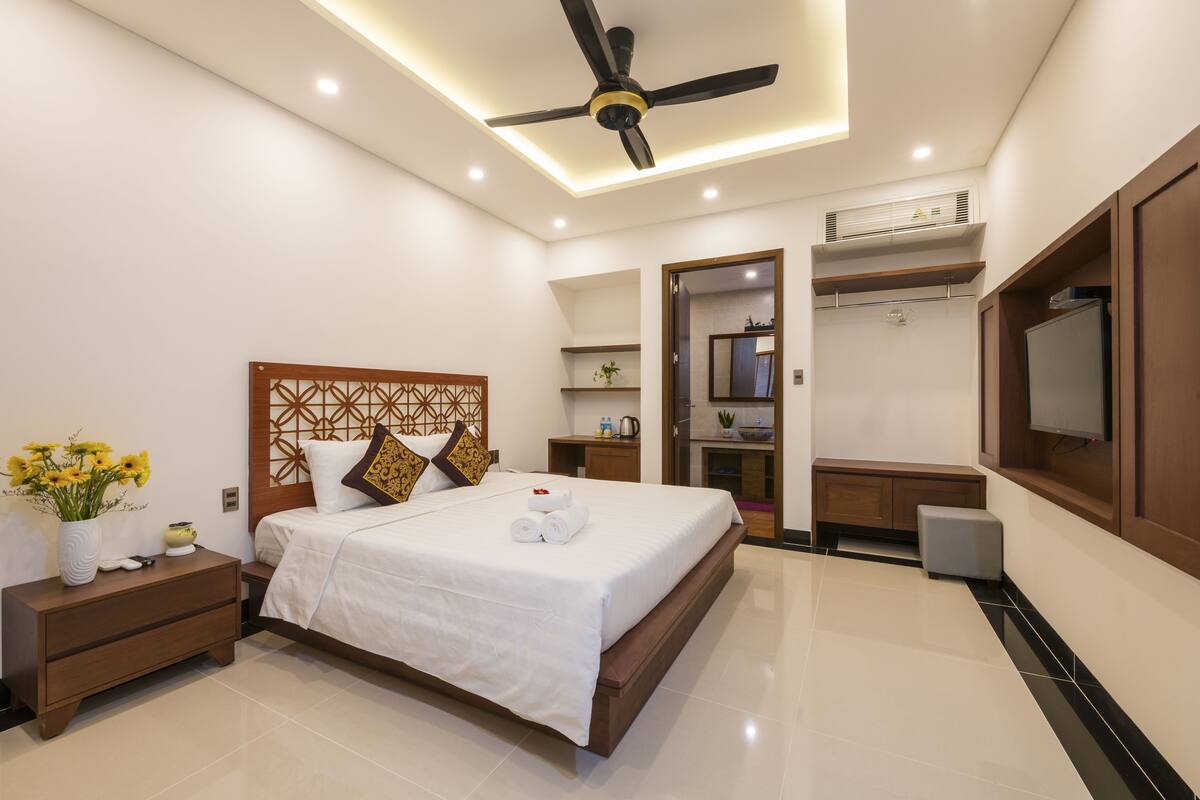 A modern hotel room with a large bed, bedside tables, a ceiling fan, and a TV.