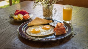 A breakfast plate with eggs, toast, bacon, and fruit on a wooden table. - Sanur Lodge (Denpasar)
