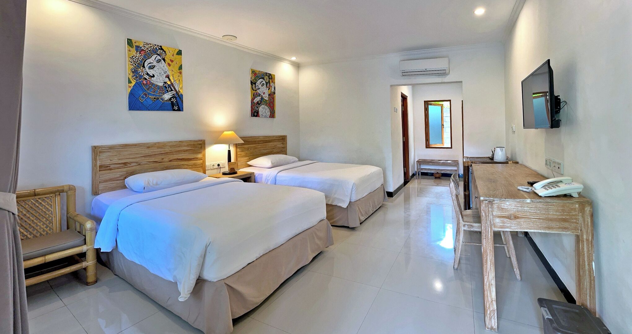 A hotel room with two beds, a wooden desk, a chair, a TV, and artwork on the walls.