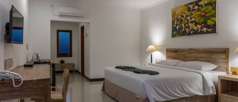 A hotel room with a bed, bedside table, lamp, desk with a telephone, and a painting on the wall.