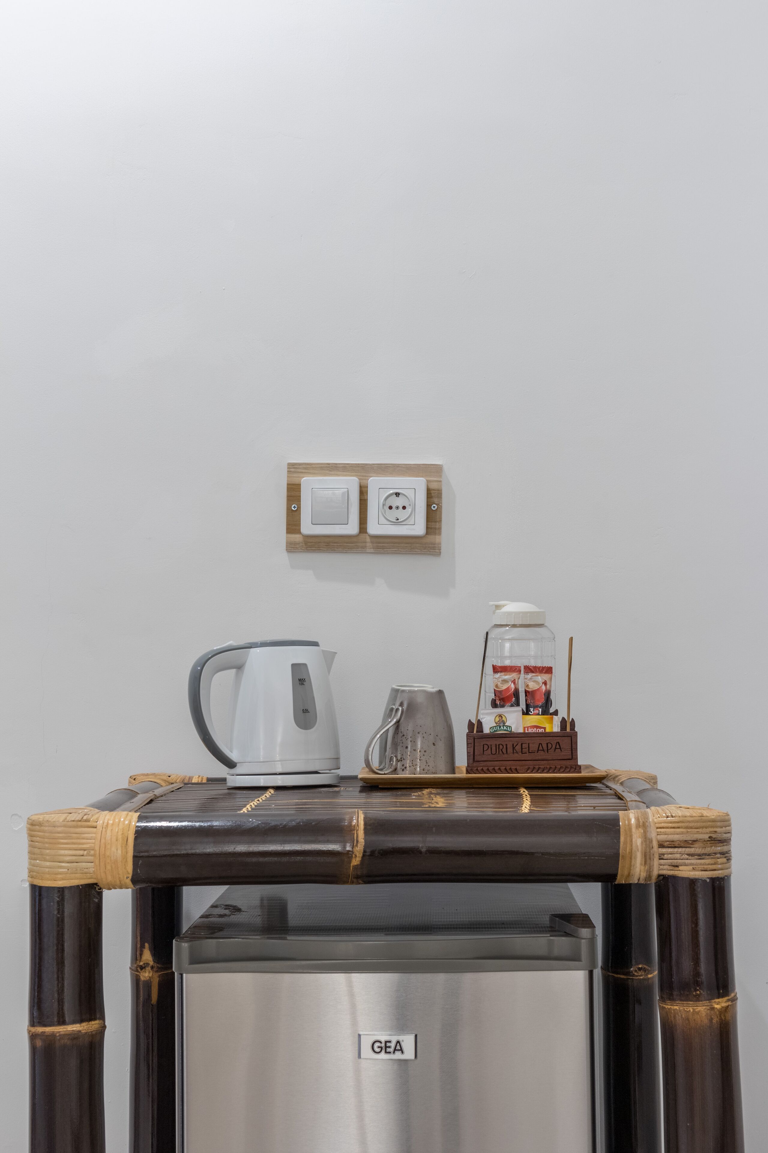 A kitchenette with a GE refrigerator, a white kettle, and a coffee maker on a bamboo table.