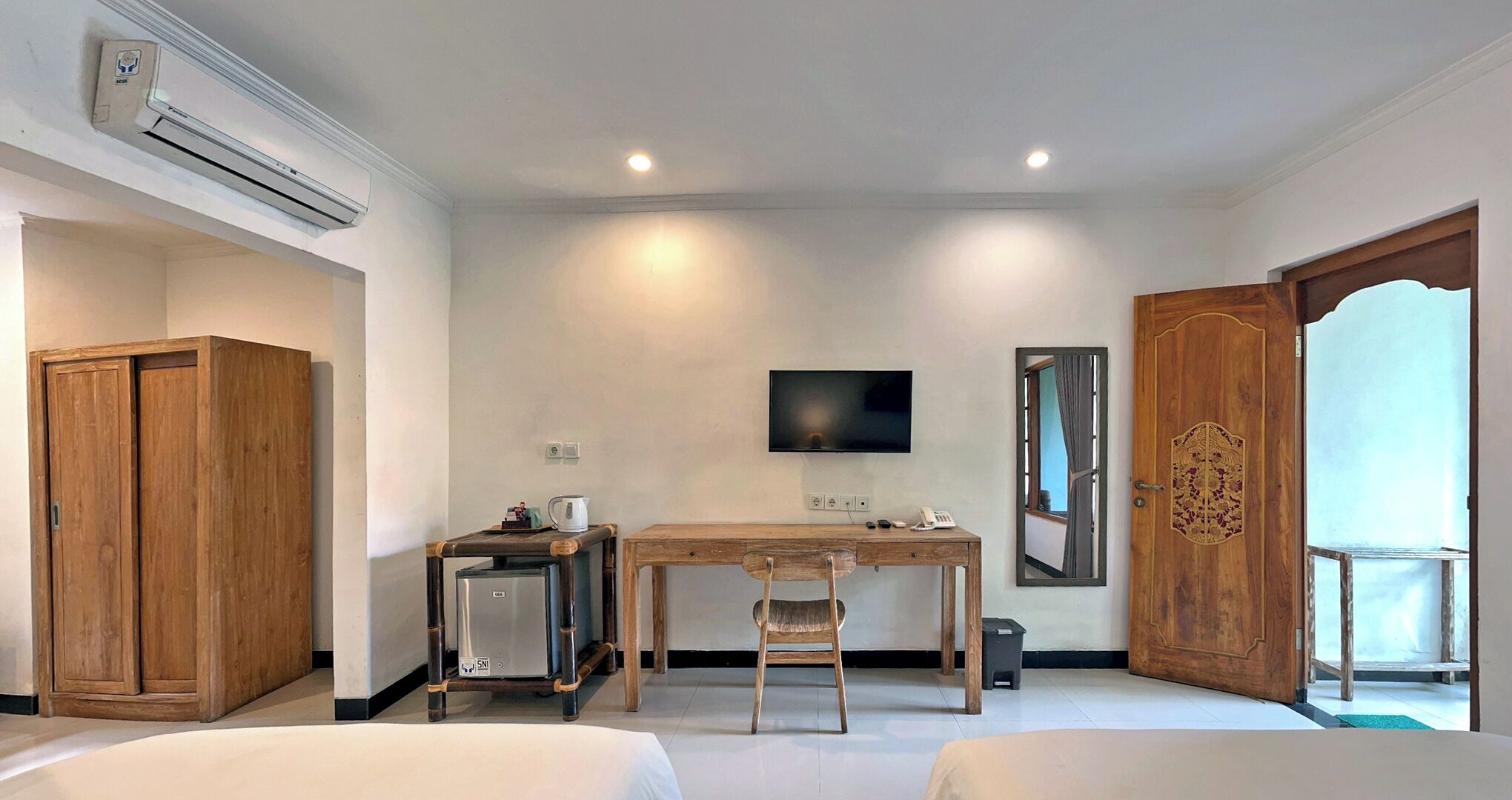 A hotel room with a bed, a desk with a chair, a TV, a wardrobe, and a door.