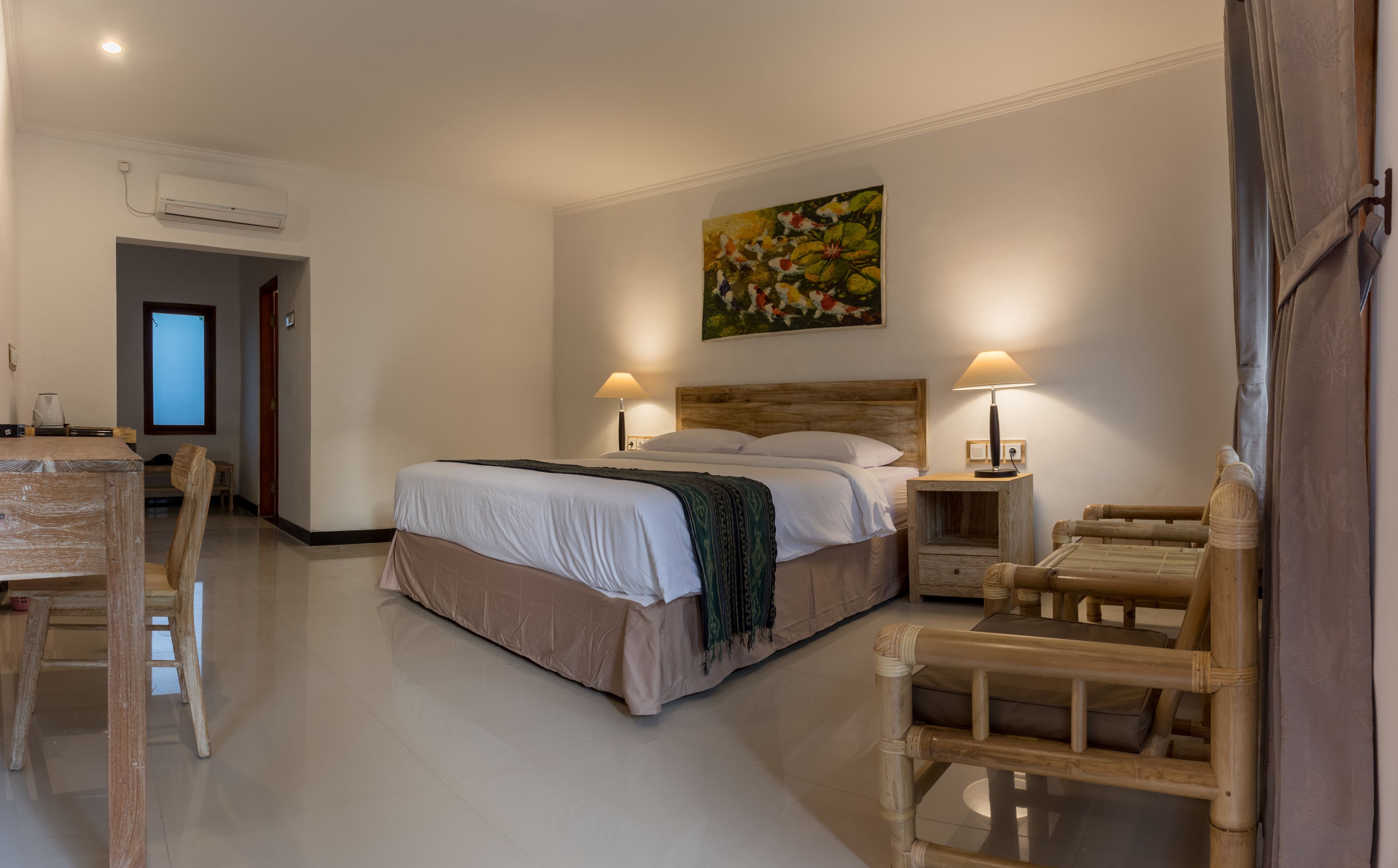 Een hotelkamer met een bed, twee nachtkastjes met lampen, een houten stoel, een bureau met stoel en een airconditioner.
