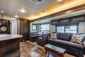 A compact RV interior with a kitchenette, seating area, and a window providing a view of the outside.