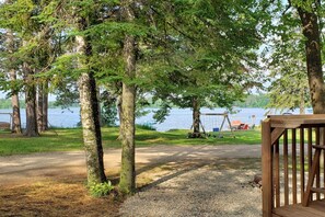 A gravel path leading to a wooden deck overlooking a lake, with trees and a swing set visible in the background.