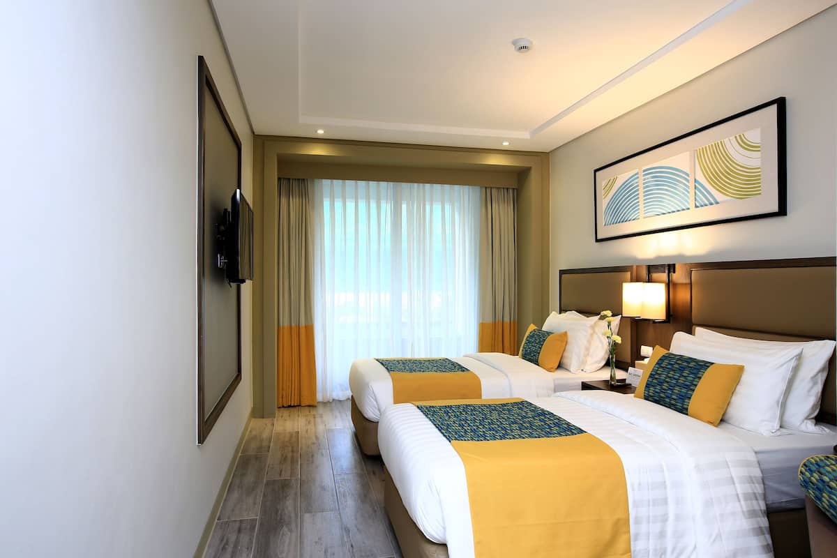 Habitació d'hotel amb dos llits, televisió de pantalla plana, un quadre i una finestra gran amb cortines.