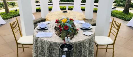 A round table set for a meal with a patterned tablecloth, gold chairs, and a floral centerpiece.