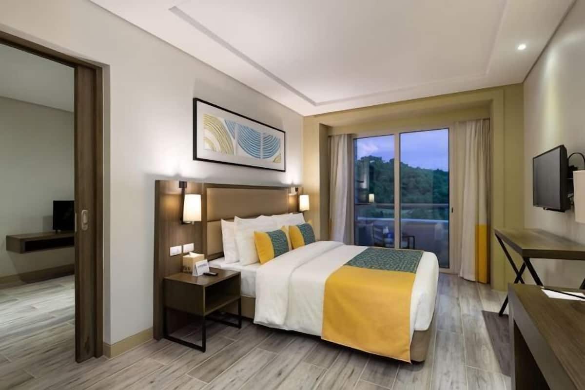 Habitació d'hotel amb un llit, taules de nit, televisió i una finestra gran amb vistes.