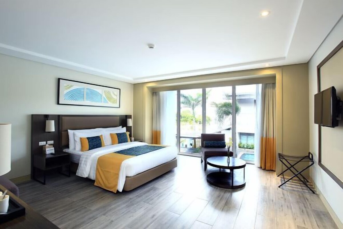 A hotel room with a large bed, a desk, a chair, a TV, and a balcony with a view.