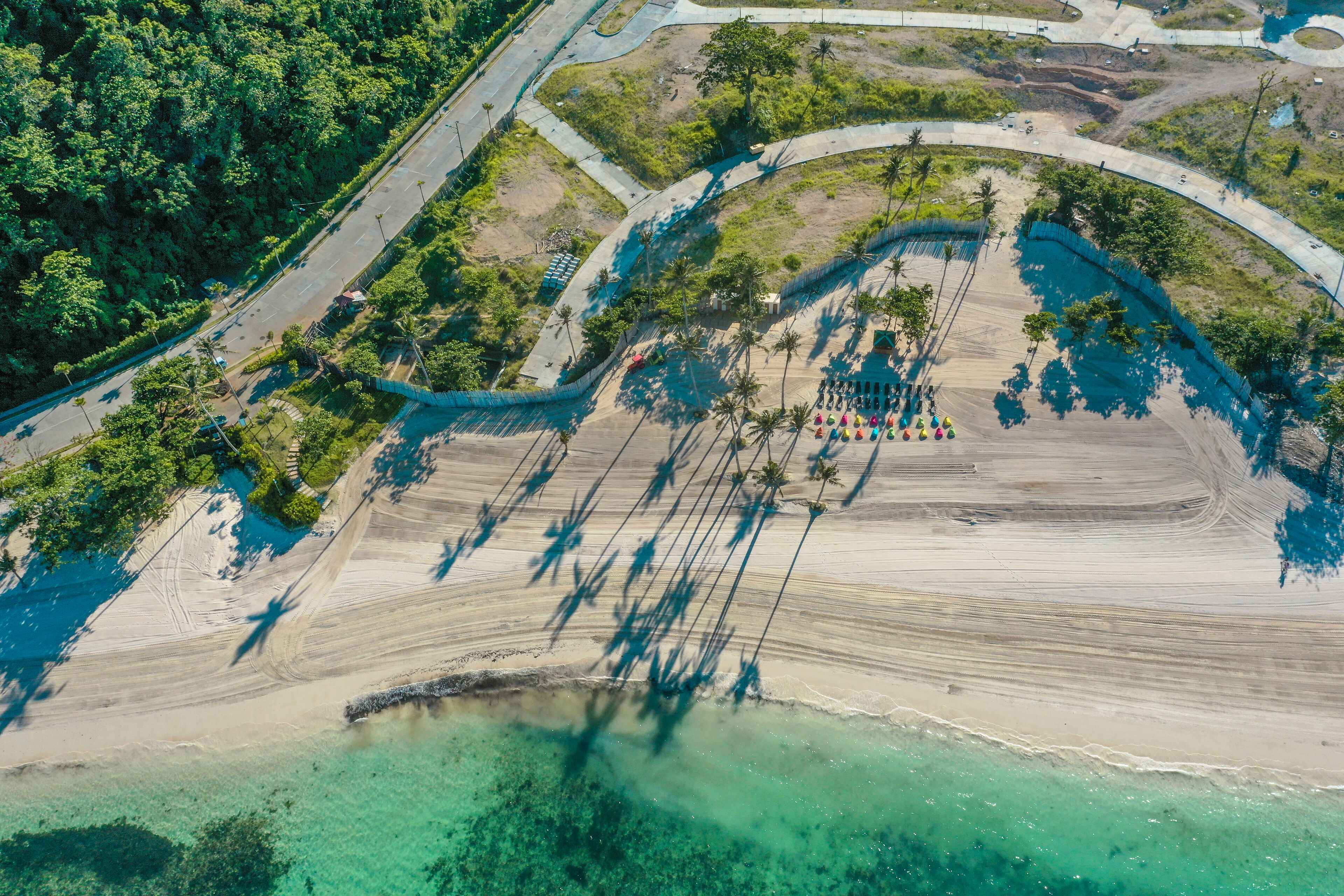 Vista aérea de una zona costera con playa, agua cristalina y una carretera serpenteando por el paisaje.