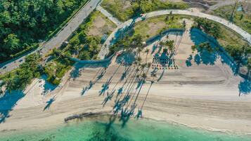Vista aérea de una zona costera con playa, agua cristalina y una carretera serpenteando por el paisaje.