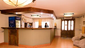 A reception area with a wooden counter, a clock, and a person standing behind it. - Gostinyi Dvor Galirad (Oskemen)