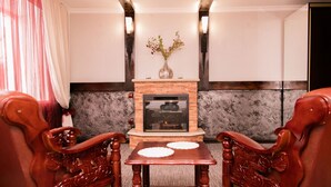 A room with a fireplace, two wooden chairs, a small table, and a decorative vase. - Gostinyi Dvor Galirad (Oskemen)