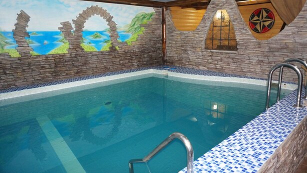 A swimming pool with stone walls and a mural of a coastal scene. - Gostinyi Dvor Galirad (Oskemen)