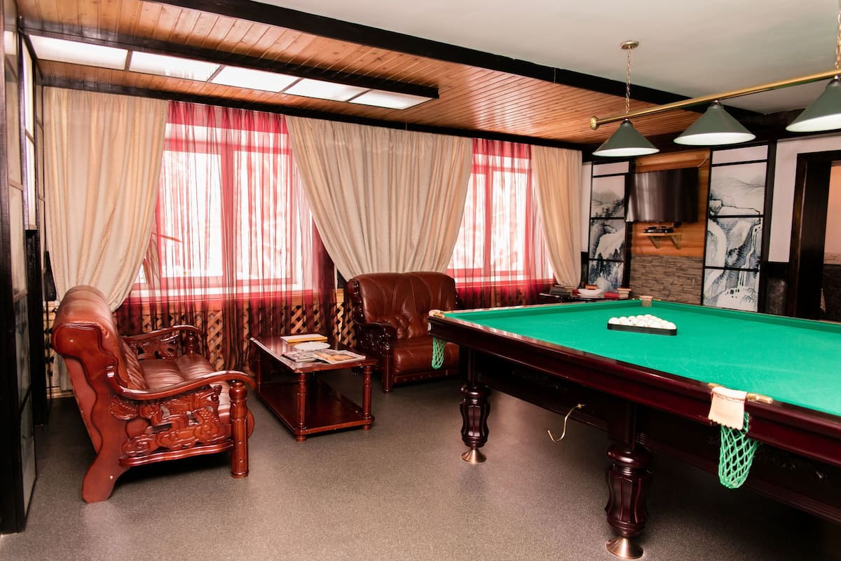 A billiards room with a pool table, leather armchairs, and a sofa.