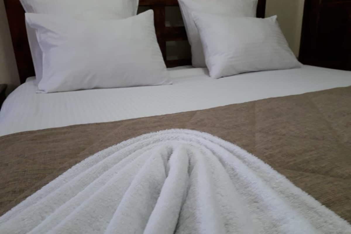 A neatly made bed with white linens and a brown throw blanket.