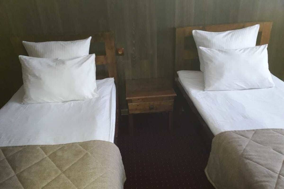 Two single beds with white linens and pillows, a wooden bench, and a carpeted floor.