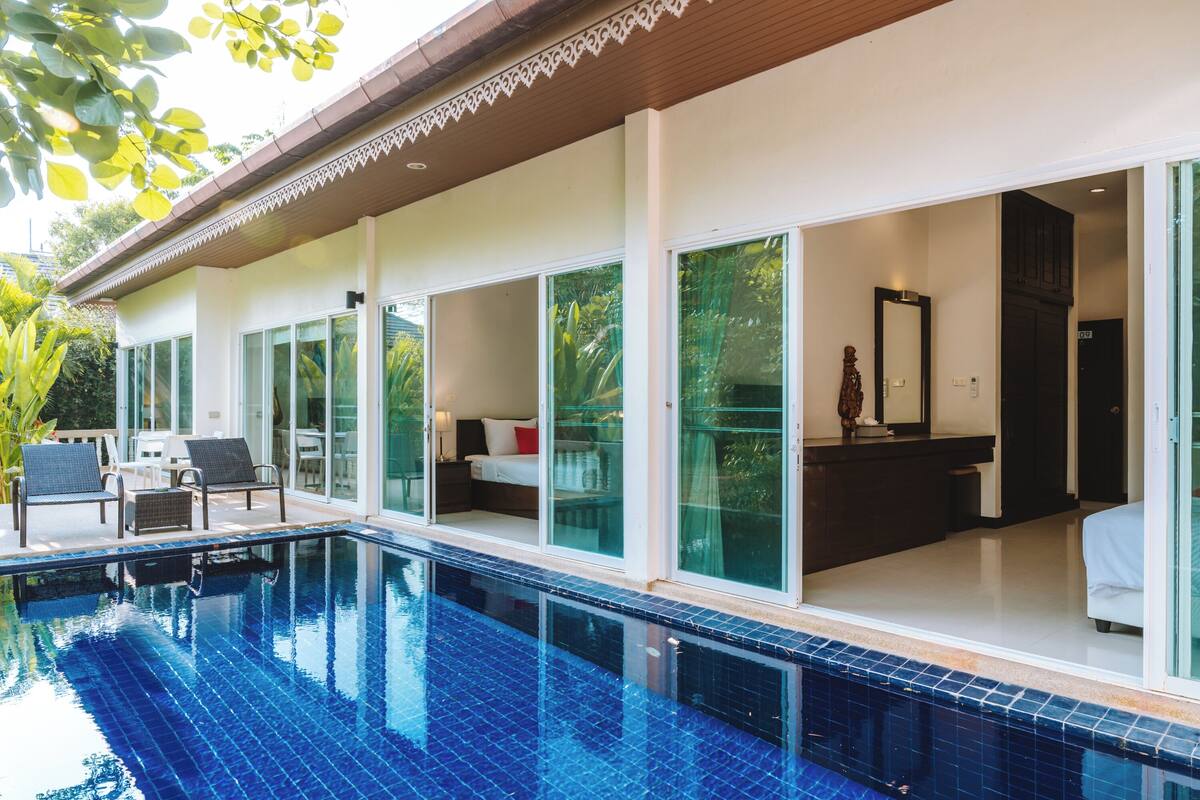A modern hotel with a swimming pool, large glass doors leading to rooms, and a balcony with seating.