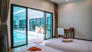 A hotel room with two beds, a desk, and a view of an outdoor swimming pool. - Layantara Villas (Thep Krasattri)