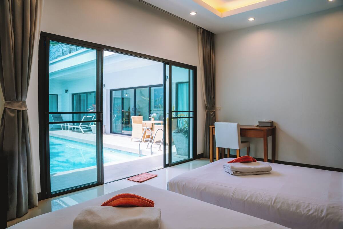 A hotel room with two beds, a desk, and a view of an outdoor swimming pool.