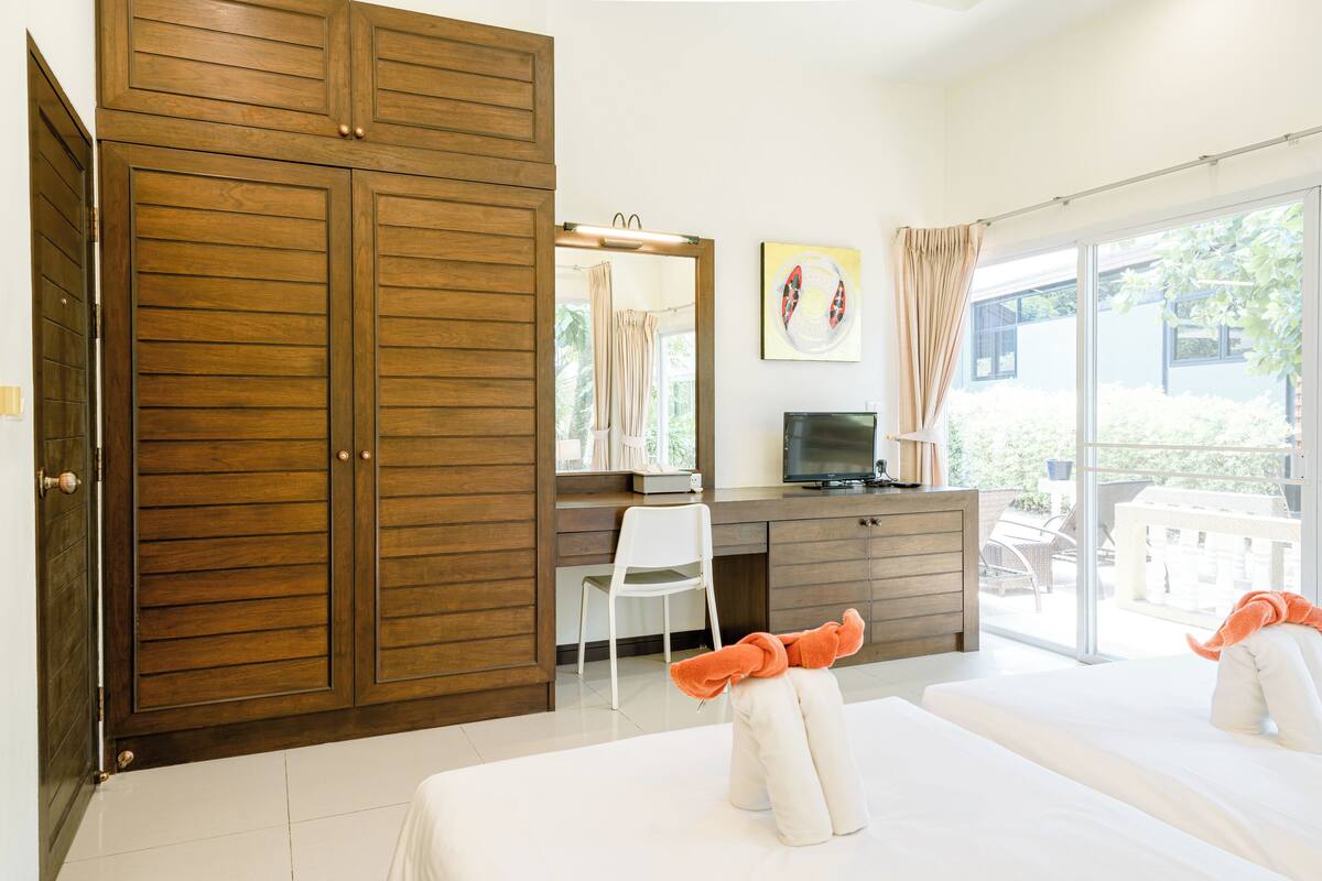 A hotel room with a wooden wardrobe, a desk with a chair, a television, and two beds.