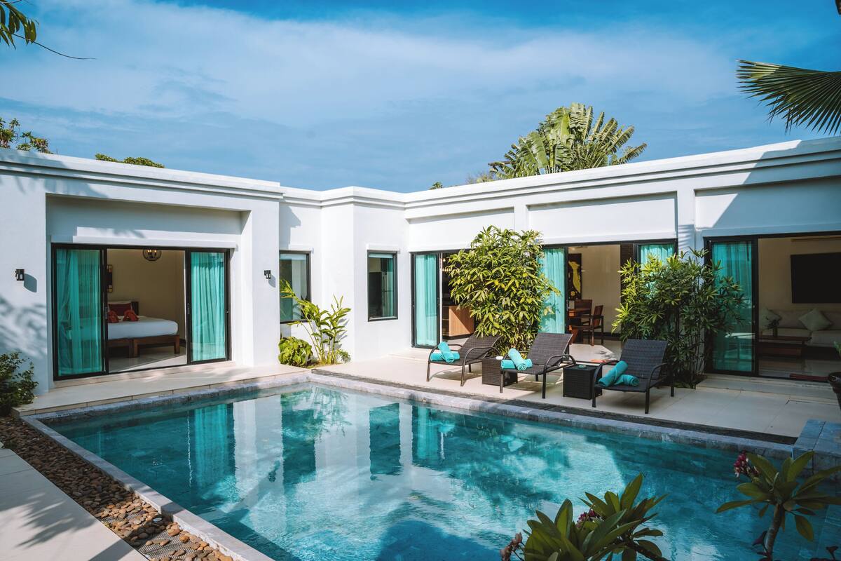 A modern poolside area with a clear pool, outdoor seating, and a well-maintained garden.