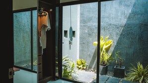 A modern bathroom with a glass door leading to a small outdoor garden area with plants and a stone pathway. - Layantara Villas (Thep Krasattri)