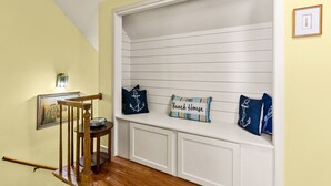A hallway with a wooden chair, a bench with nautical-themed cushions, and a framed picture on the wall. - Comfortable 2 bedroom Beach Home located on quiet street (Saint Simons Island)