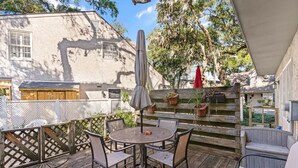 A wooden deck with a round table and chairs, a covered umbrella, and a wooden fence. - Comfortable 2 bedroom Beach Home located on quiet street (Saint Simons Island)